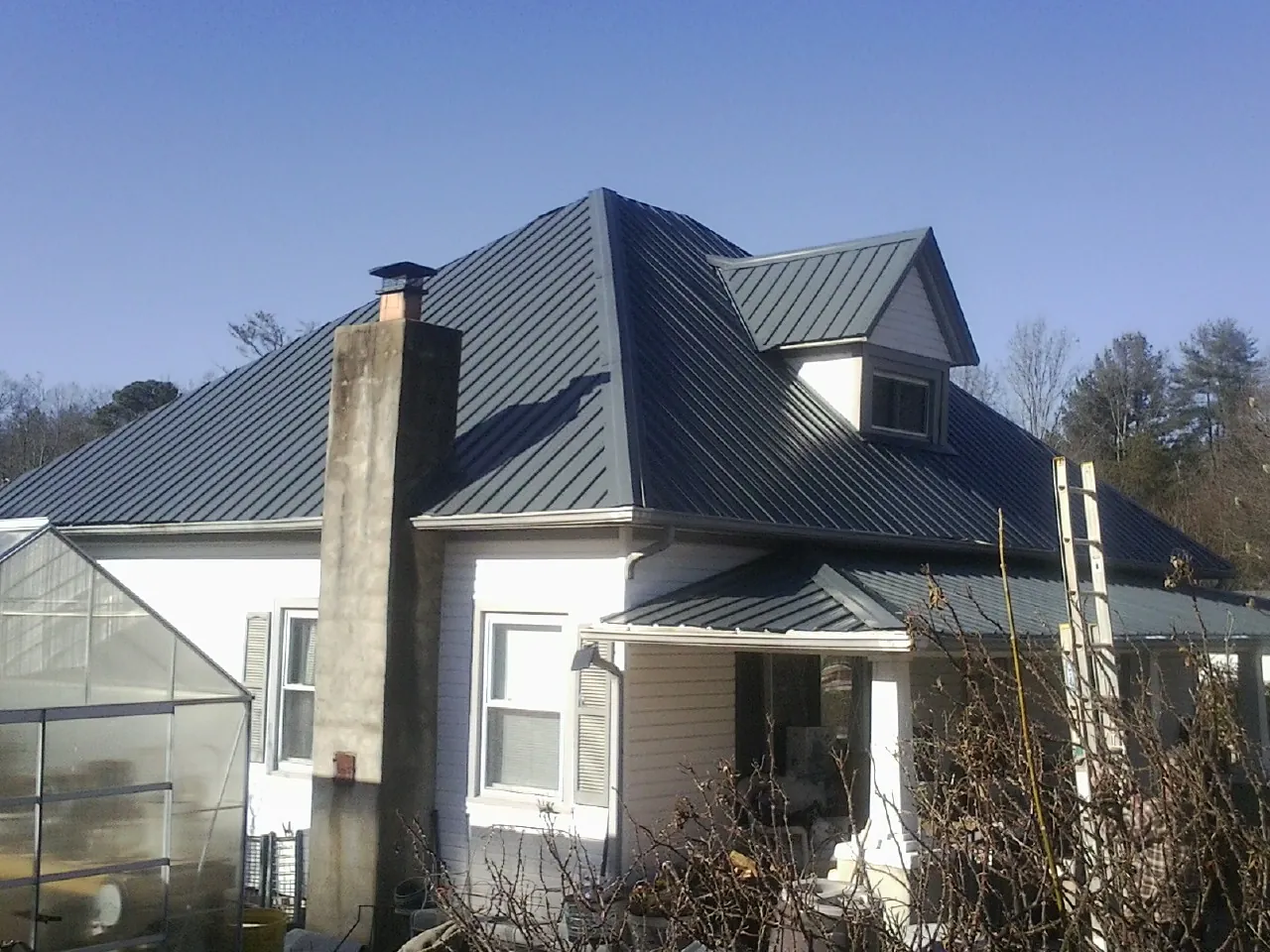 Dark blue standing seam metal roof on a white farmhouse with dormer — Slate & Tile Roof Repair by Roofing Brothers in Ranson