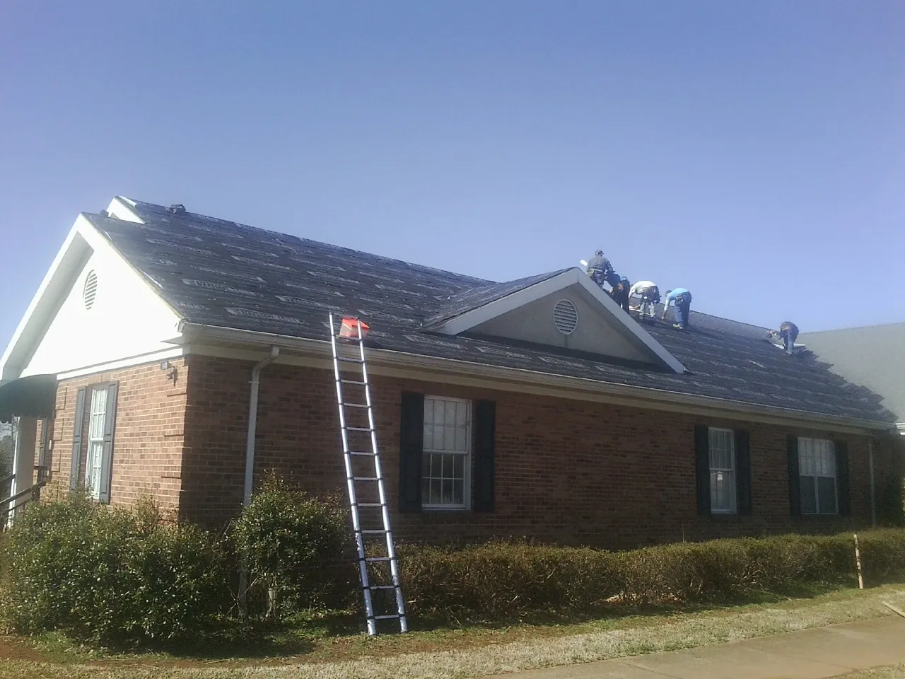 Crew tearing shingles off a brick ranch roof with a ladder set — Emergency Roof Repair work by our crew in Ranson