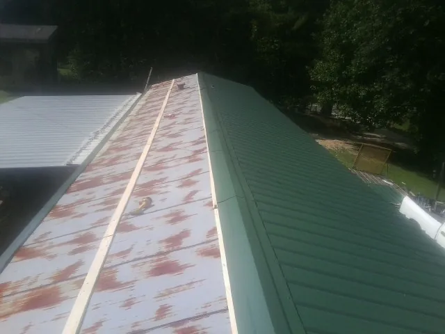 Old rusted panels beside newly installed green metal roofing — Wind Damage Roof Repair by Roofing Brothers in Ranson