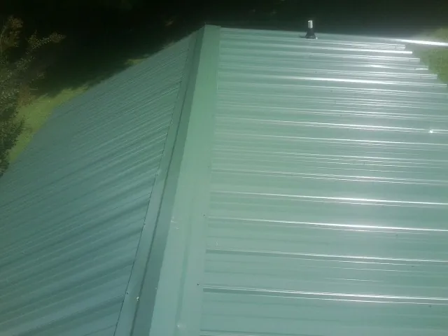 New green metal panels meeting at the ridge of a roof — Flat Roof Repair work by our crew in Ranson