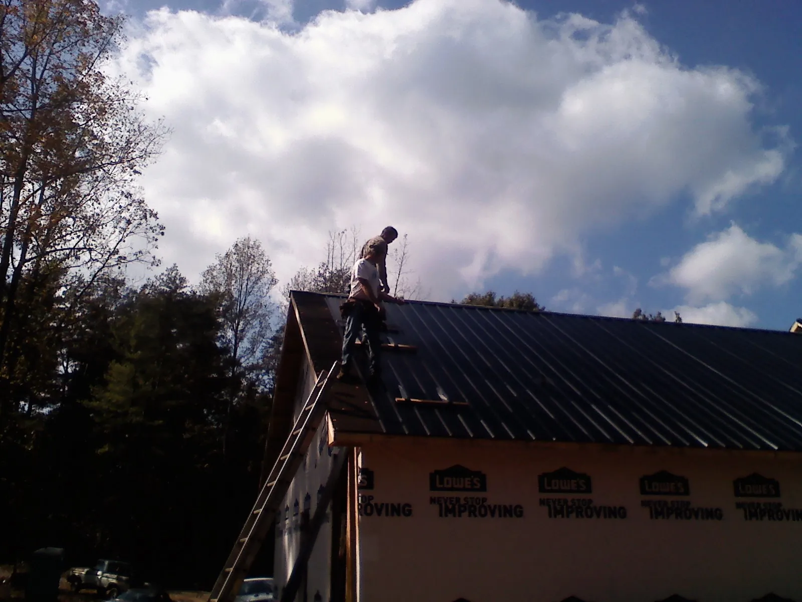 Roofer fastening dark metal panels high against a cloudy sky, from a Roof Inspection job in Ranson